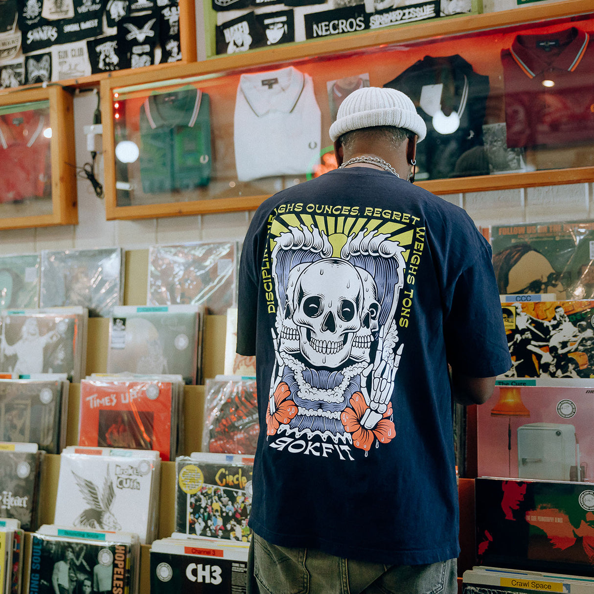 Male model in record store wearing unisex Street Tee with 'Discipline Weighs Ounces, Regret Weighs Tons' graphic