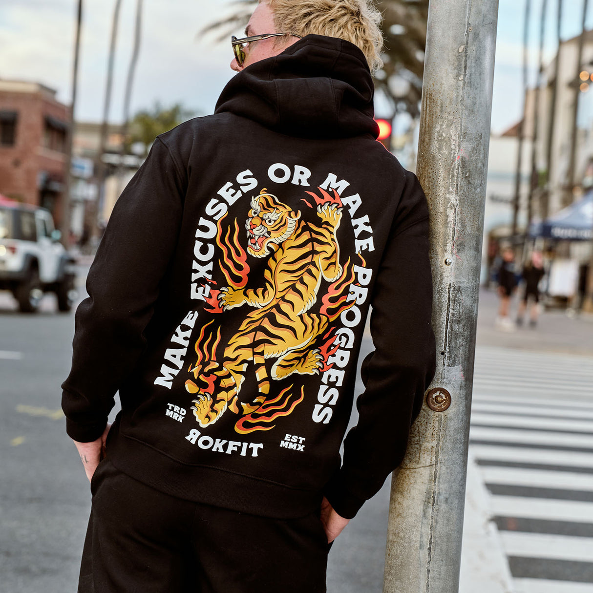 Male model outdoors wearing hoody with 'Make Excuses or Make Progress' graphic