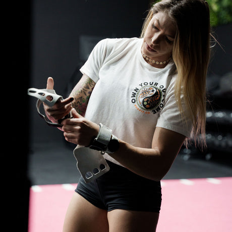 Female model in a gym wearing white crop top with 'Excuses or Reasons' graphic