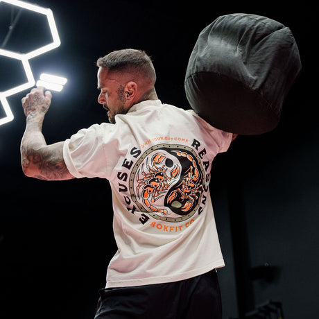 Male model doing a weighted ball throw in a gym wearing Street Tee with 'Excuses or Reasons' graphic