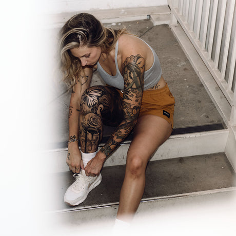 Female model tying shoes wearing women's gold Hybrid Shorts